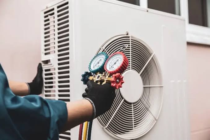 Gloved technician checking refrigerant pressure gauges beside an outdoor air conditioner