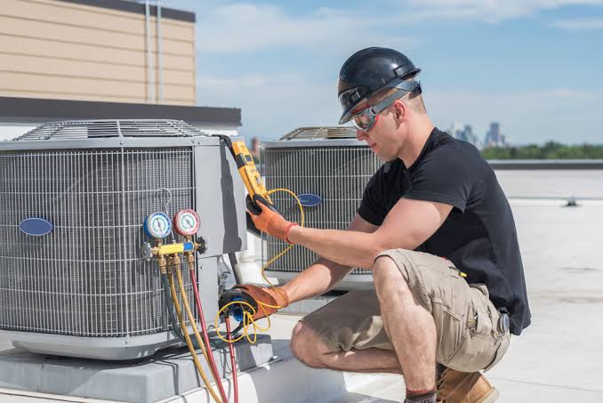 Technician inspecting rooftop air conditioning equipment with pressure gauges and an electrical meter