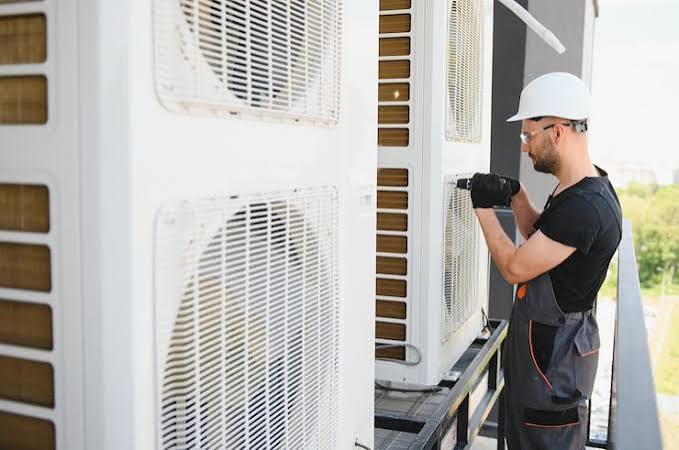 Technician using a drill while working on a large outdoor air conditioning system